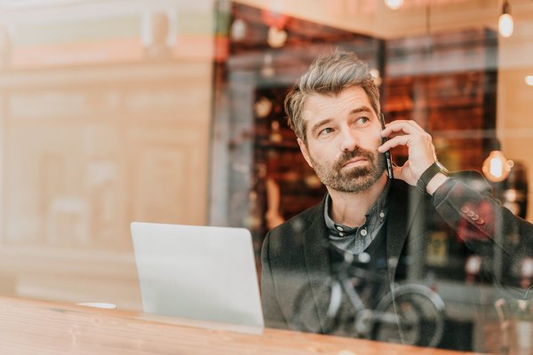 Wahler Versicherungen, Firmenrechtsschutzversicherung: Mann hinter Fensterscheiben in einem Cafe sitzend und telefonierend