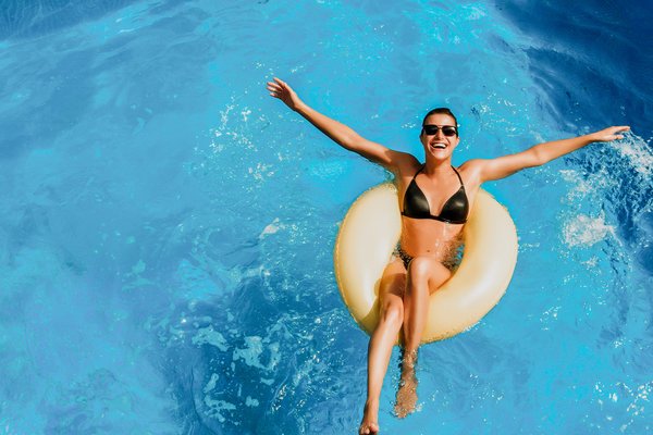 Wahler Magazinartikel: Swimmingpool – alles cool? Frau liegt fröhlich auf gelbem Schwimmreif im Pool