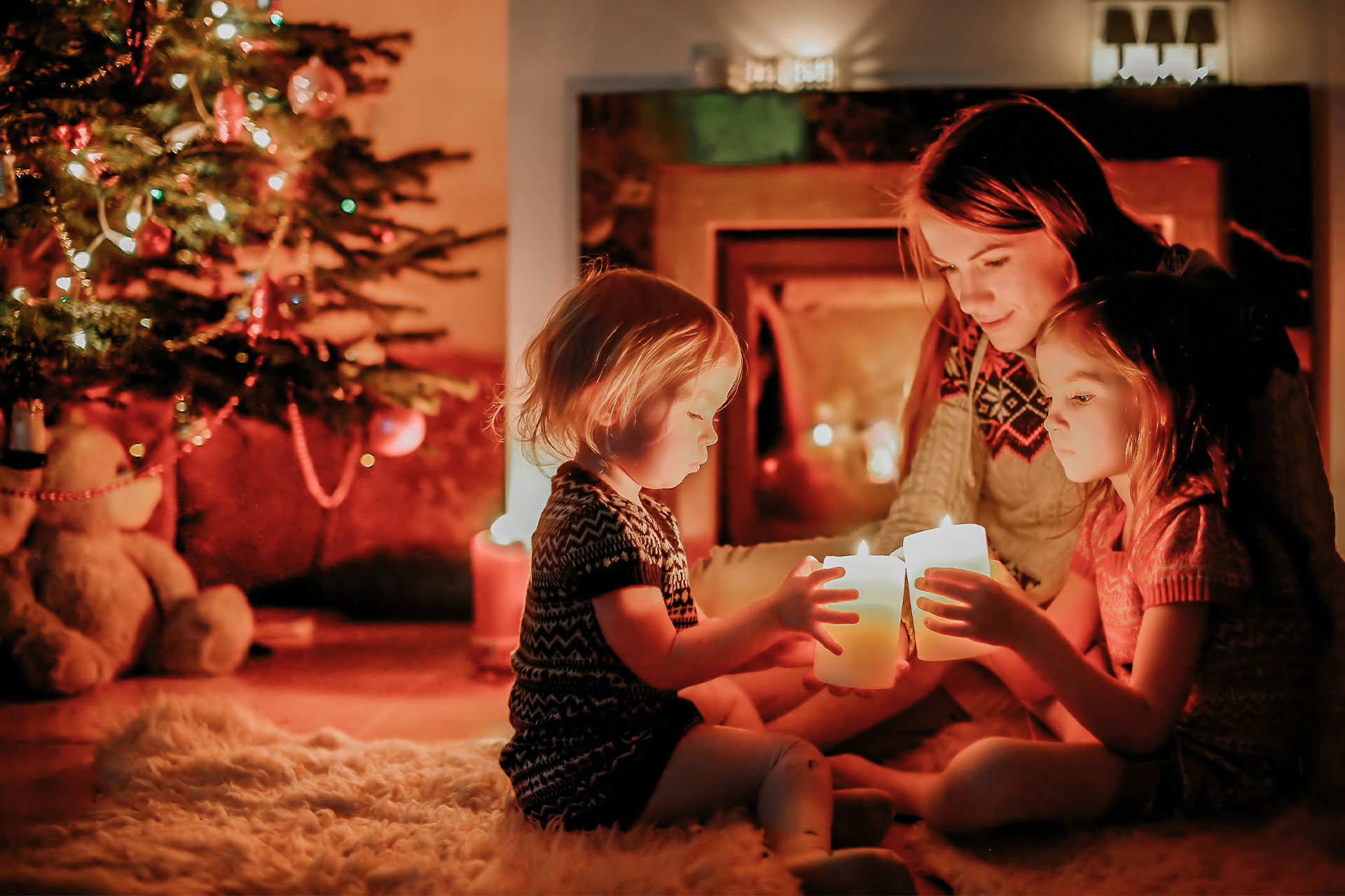 Tipps für schadenfreies Weihnachten - Mutter sitzt mit zwei Kindern unterm Weihanchtsbaum und zündet Kerzen an